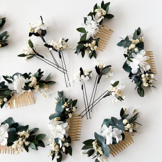 A set of white and green floral hair combs arranged on a clean white background. Each comb features white flowers, green leaves, and small cream accents attached to a gold-tone metal comb.