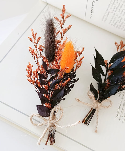 Two dried flower boutonniere with feathers on a white surface