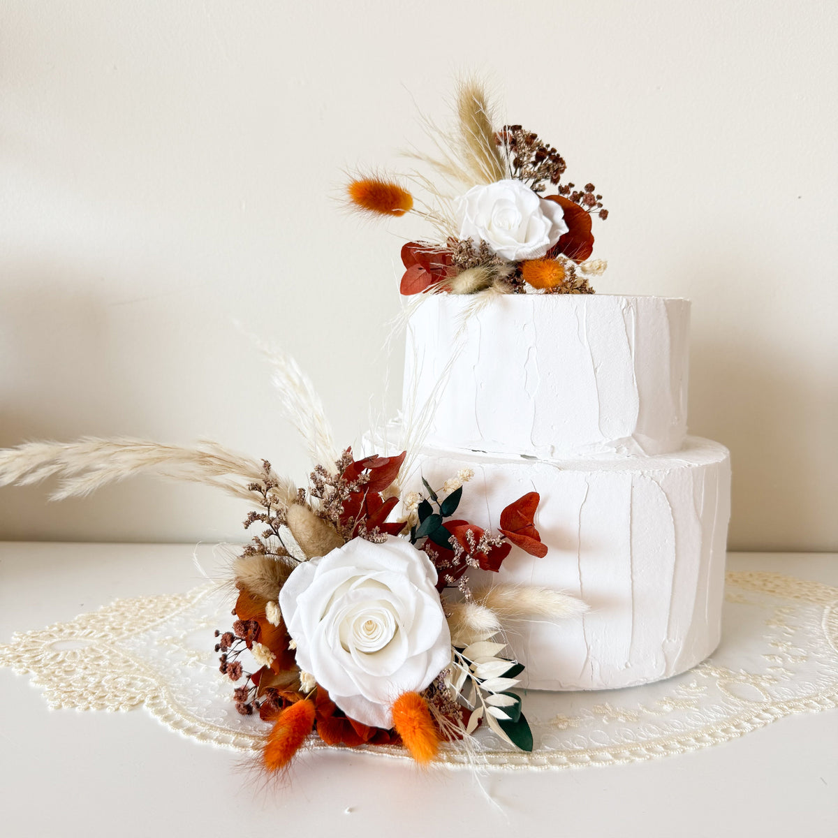 Elegant wedding cake styling with ivory roses, terracotta dried flowers and beige bunny tails in a rustic, modern botanical palette.