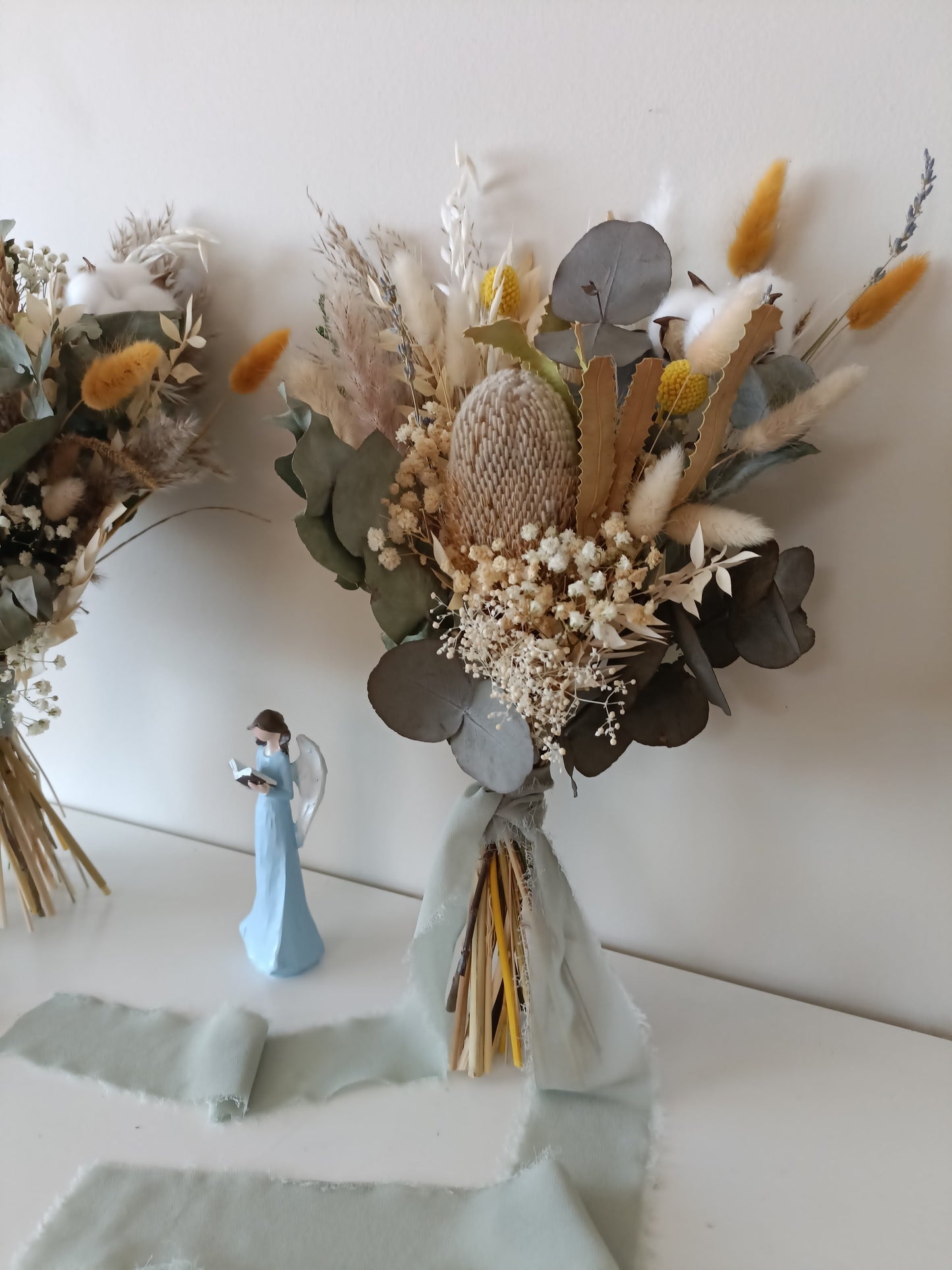 Boho dried flower bouquet in earthy tones with Australian natives and yellow pops, tied with flowing sage green ribbon.
