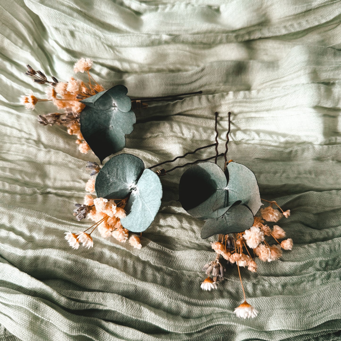 Boho wedding hair pins featuring eucalyptus leaves, white pearl stems, and soft peach preserved flowers, styled in an elegant updo