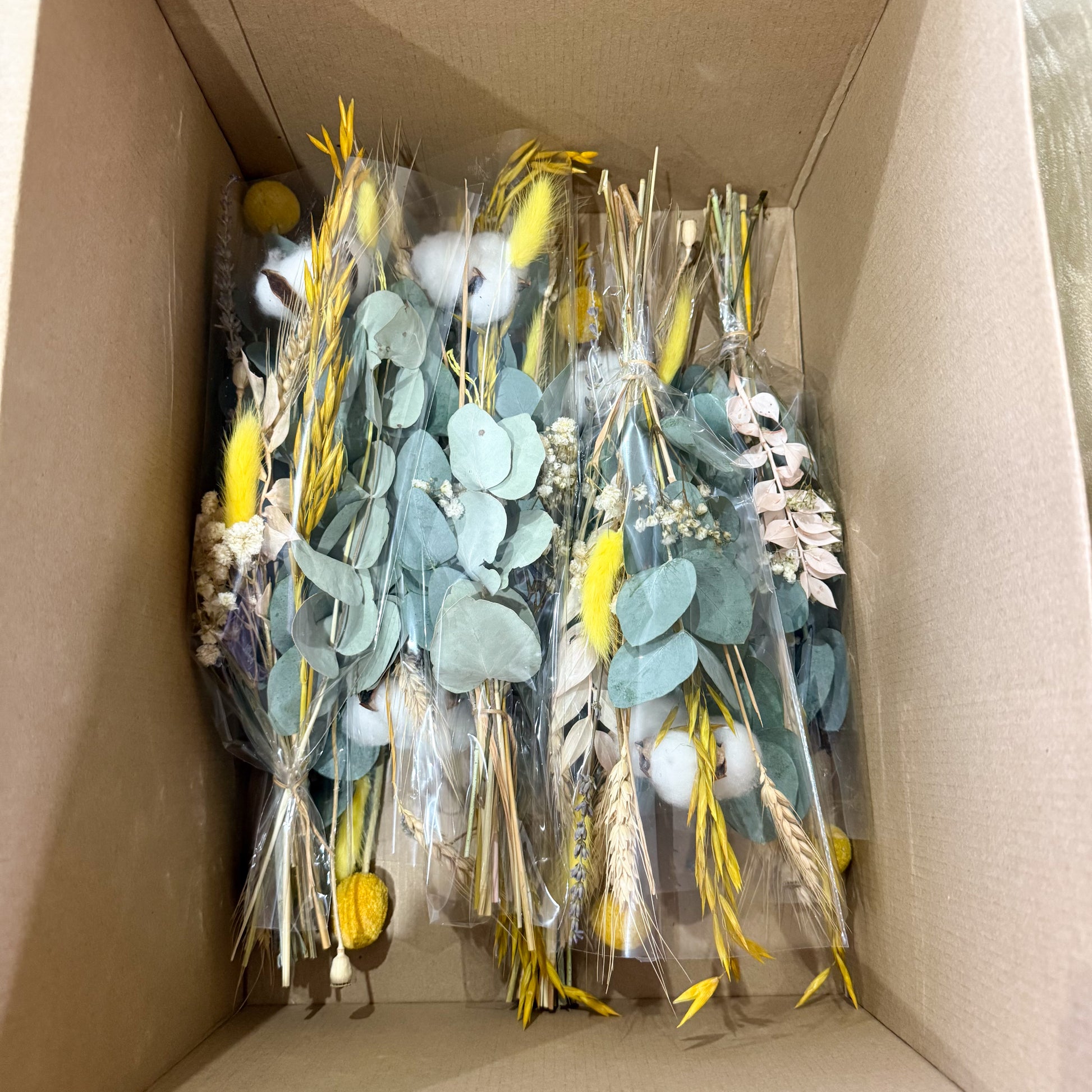 Multiple dried wedding bouquets packed in a shipping box with preserved eucalyptus, billy buttons, cotton, and wheat for delivery.
