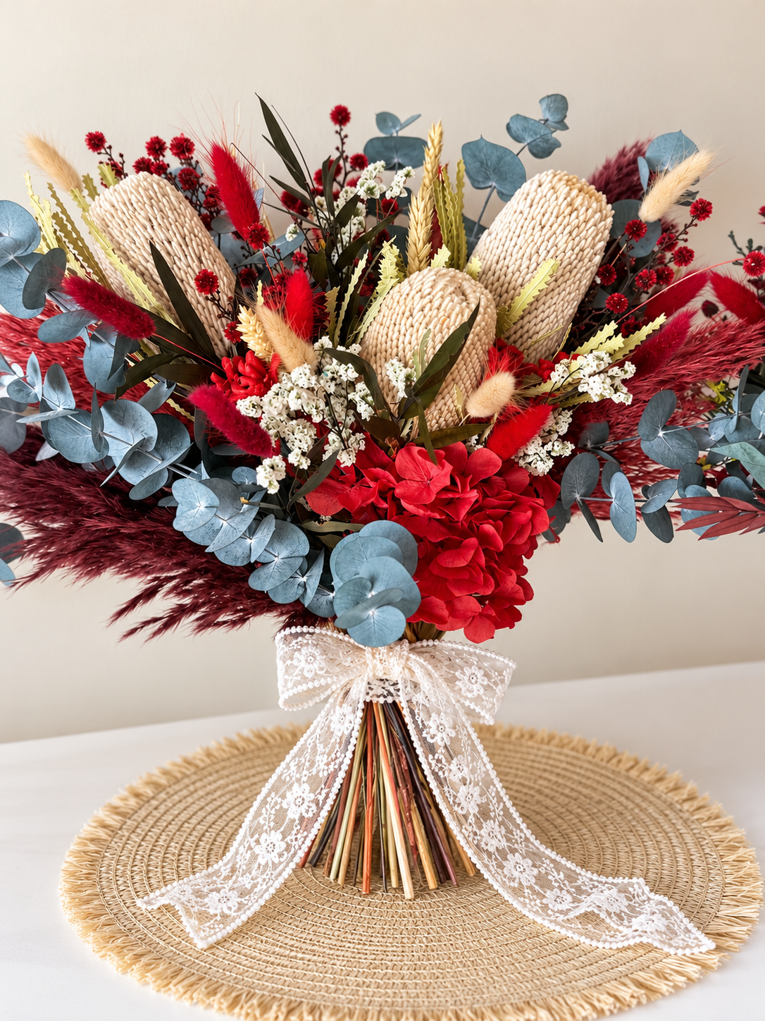 An elegant Australian native-inspired bridal bouquet with deep burgundy flowers, soft blue foliage, natural banksia and a romantic ivory lace bow. Handmade with dried and preserved botanicals for a long-lasting wedding keepsake.