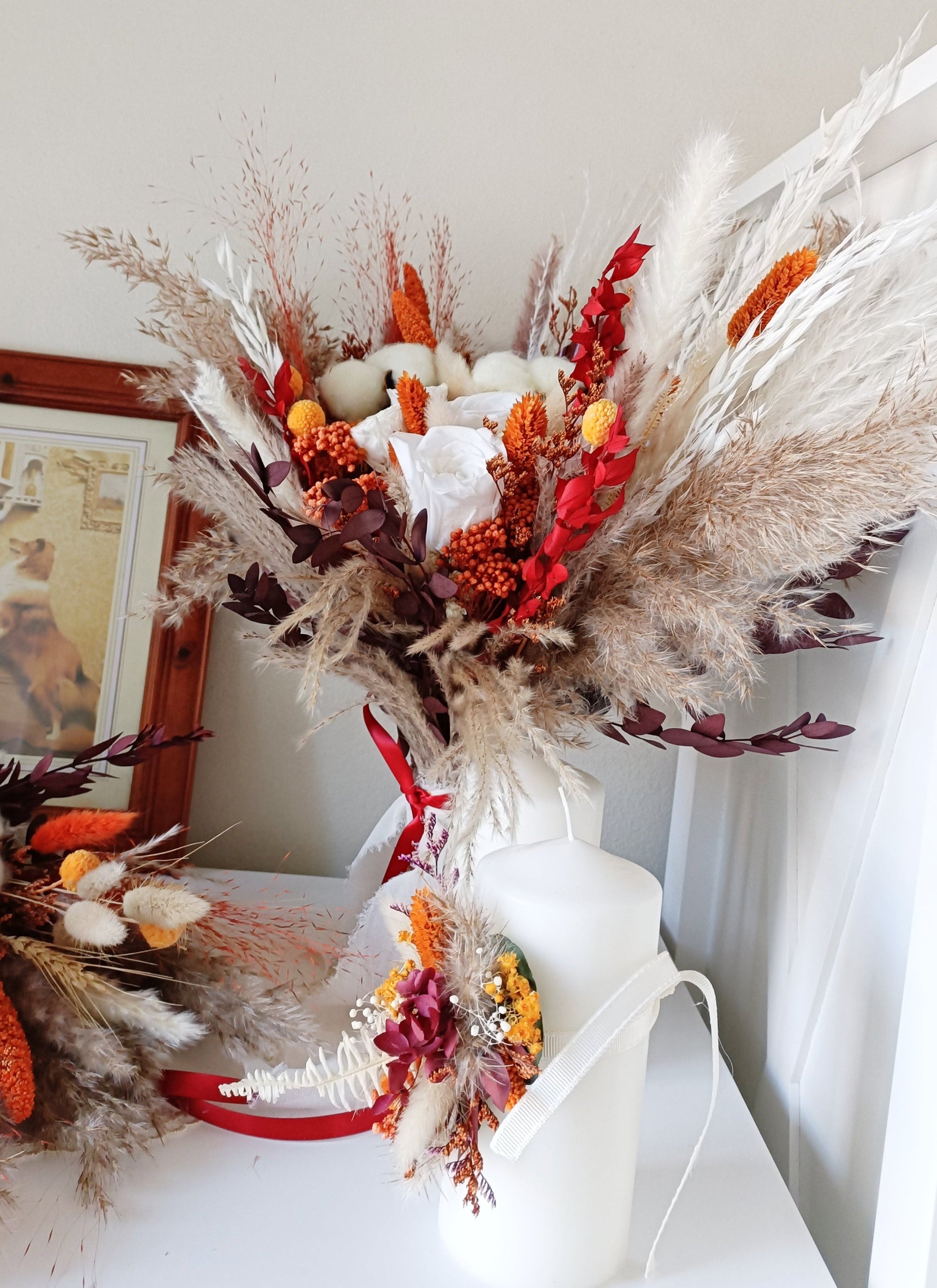 This eye-catching wedding bouquet features a bold combination of red, orange, and natural hues, crafted from a selection of dried flowers. The arrangement includes pampas grass, preserved foliage, and textured accents, offering a rustic yet vibrant look perfect for autumn weddings. Long-lasting and full of character, this bouquet adds a fiery touch to any bridal ensemble. Explore our collection for more unique and seasonal wedding bouquets.