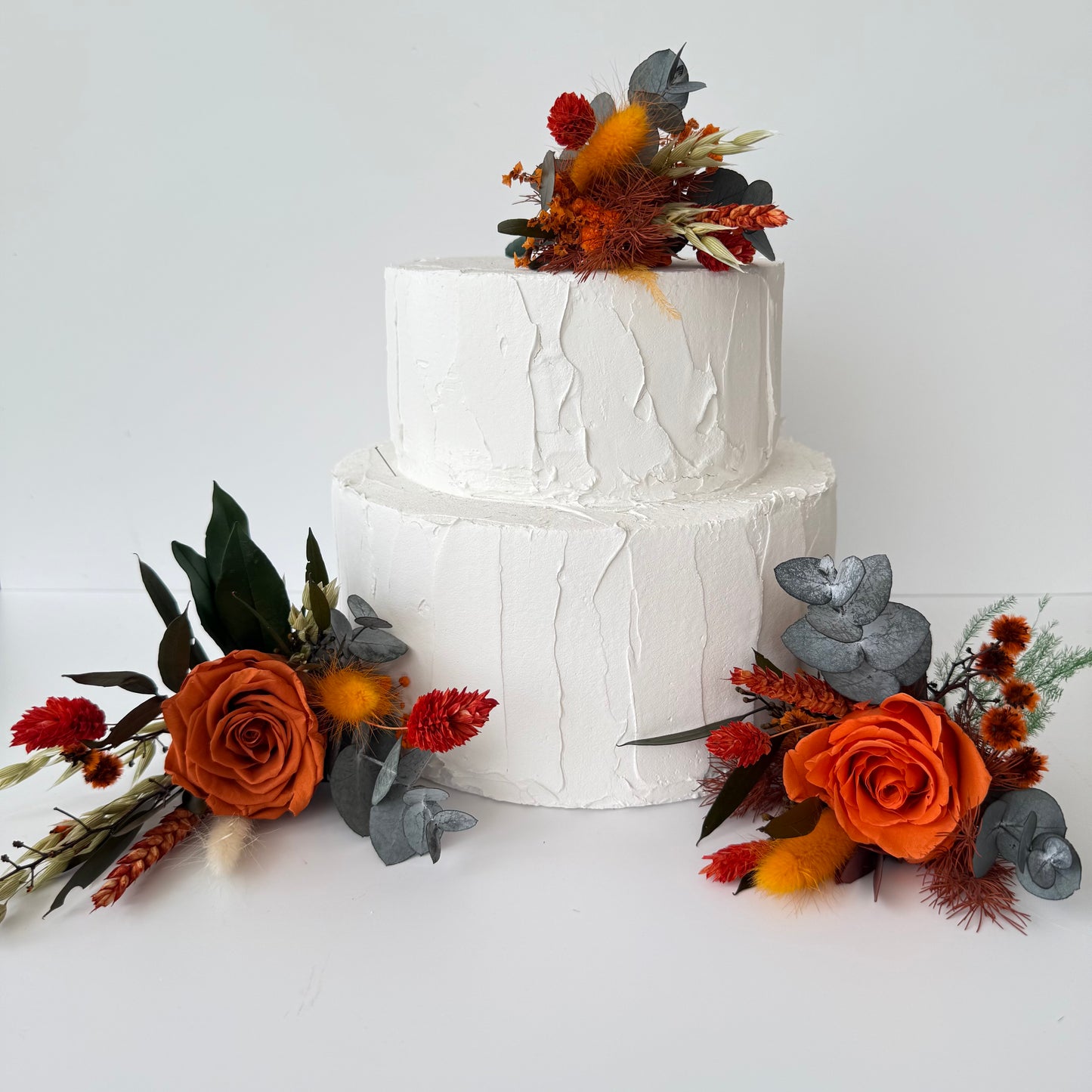 Side floral arrangement for wedding cake featuring dried burnt orange roses, eucalyptus and natural grasses.