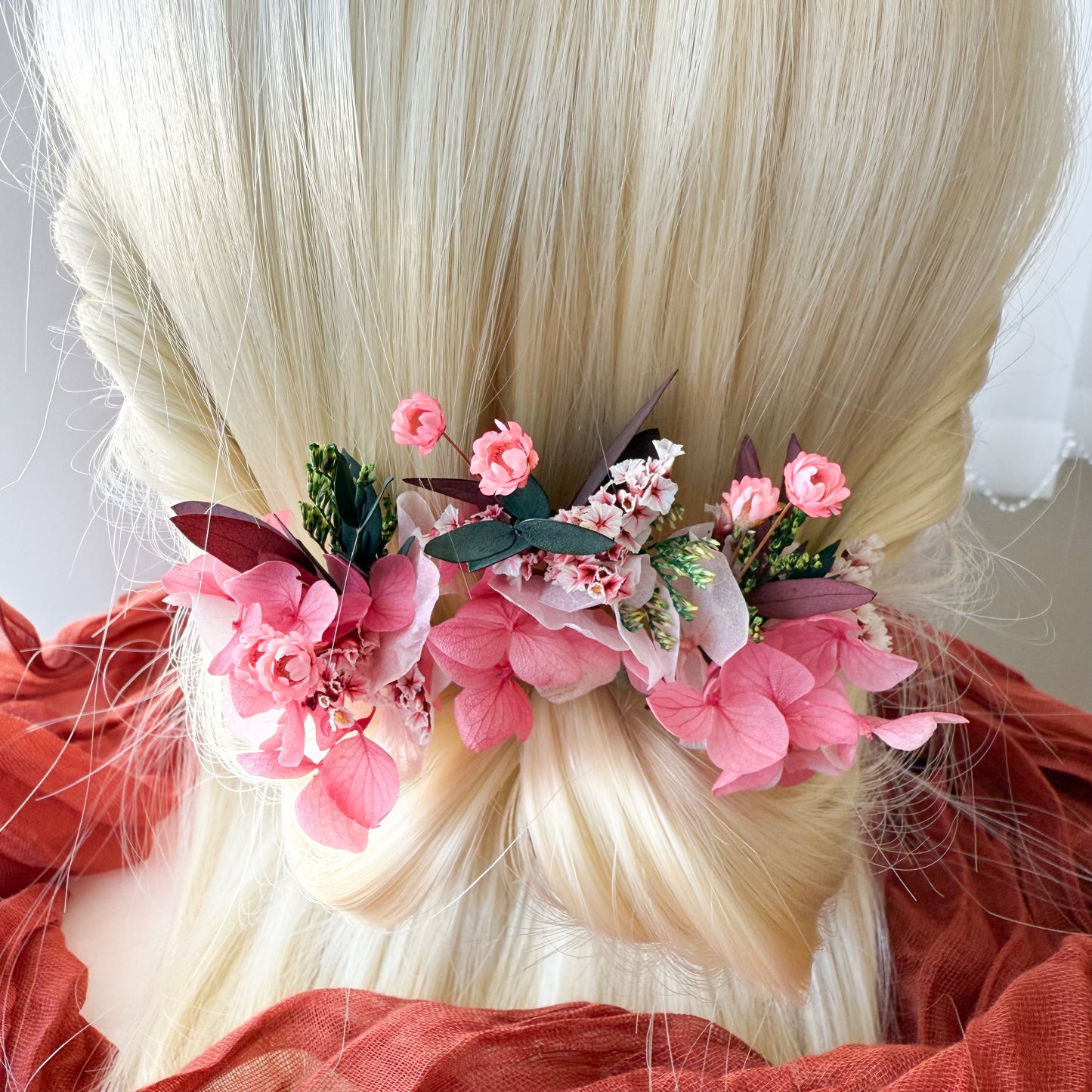 Bridal hair accessories featuring pink artificial blossoms and green foliage styled in a low twisted bun, perfect for brides or bridesmaids