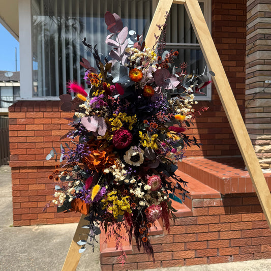 Colorful floral arrangement on a wooden stand in front of a brick building.