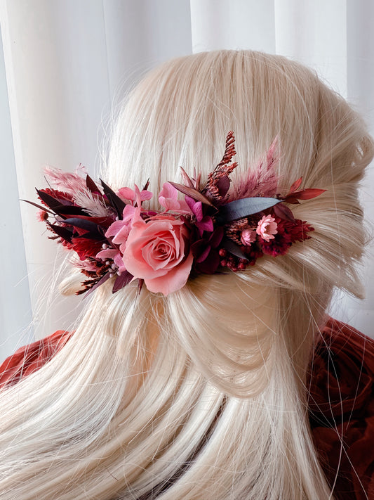 Elegant wedding hairpiece featuring coral pink preserved rose, burgundy leaves, and dried flower arrangement for boho bride hairstyle