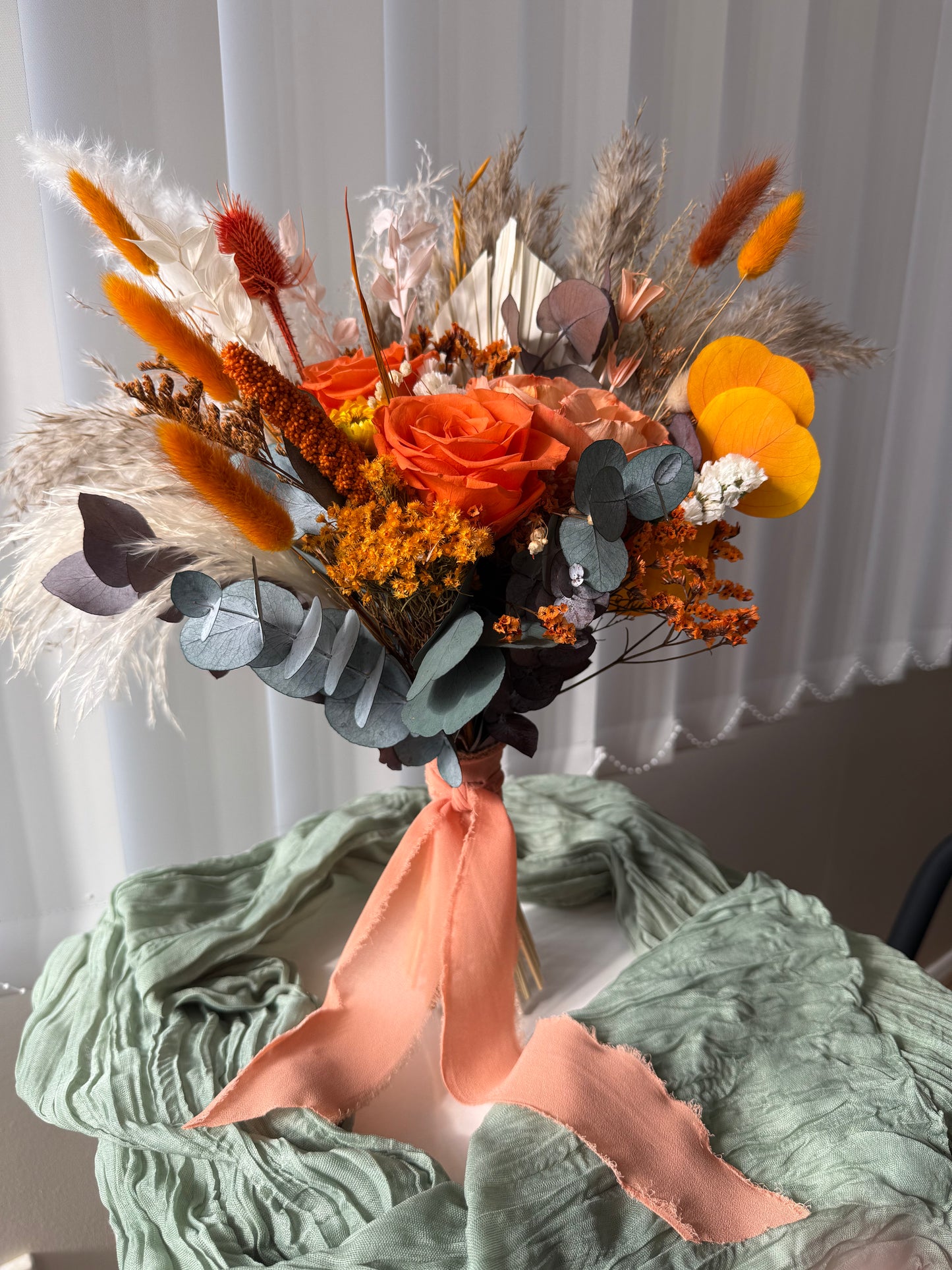 Close-up view of a boho autumn bridal bouquet with orange, yellow, and neutral dried flowers, sola wood roses, bunny tails, and eucalyptus foliage.
