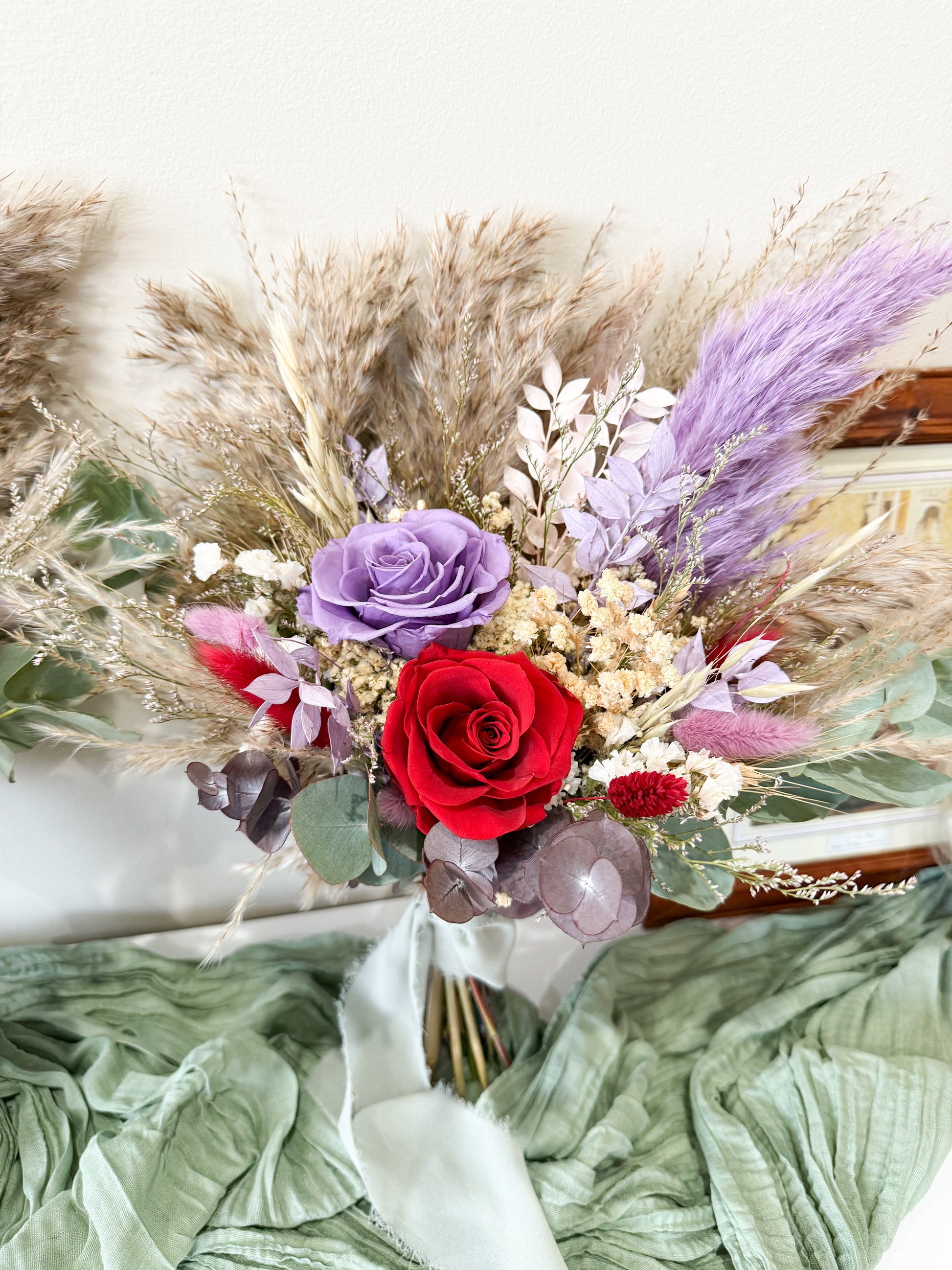 Dried bridal Bouquet of flowers with red roses, purple lavender, and greenery on a textured surface.
