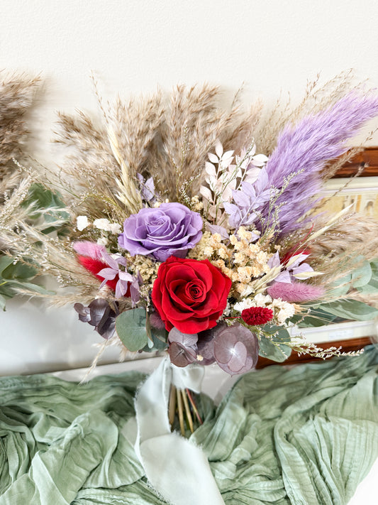 Dried bridal Bouquet of flowers with red roses, purple lavender, and greenery on a textured surface.