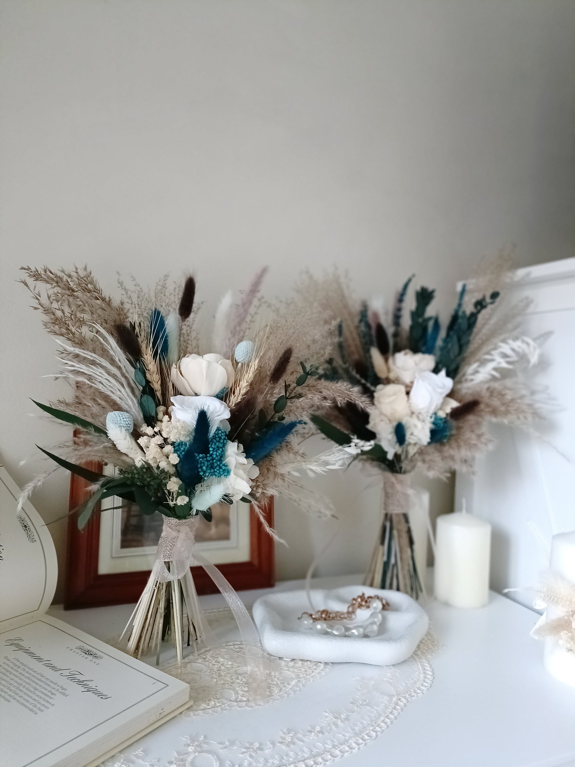 This handcrafted wedding bouquet features an exquisite blend of dried flowers, combining soft natural tones with striking blue accents. The arrangement includes pampas grass, preserved foliage, and delicate bunny tails, creating a perfect balance of rustic charm and modern elegance. Ideal for a boho-themed wedding, this long-lasting bouquet adds a touch of timeless beauty to your special day. Explore our collection for more unique bridal bouquets and wedding decor ideas.