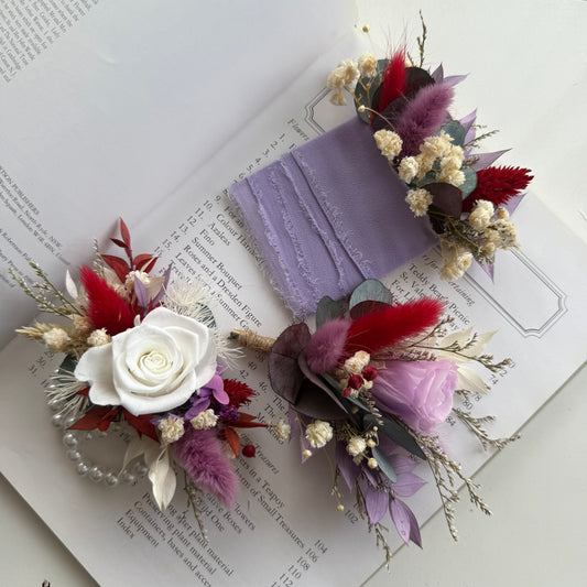 Floral groom`s accessories with a white rose and red and purple flowers on an open book.
