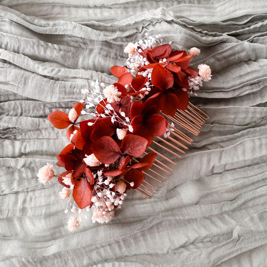 Floral hair comb with burnt red flowers and small white buds on a textured gray fabric background