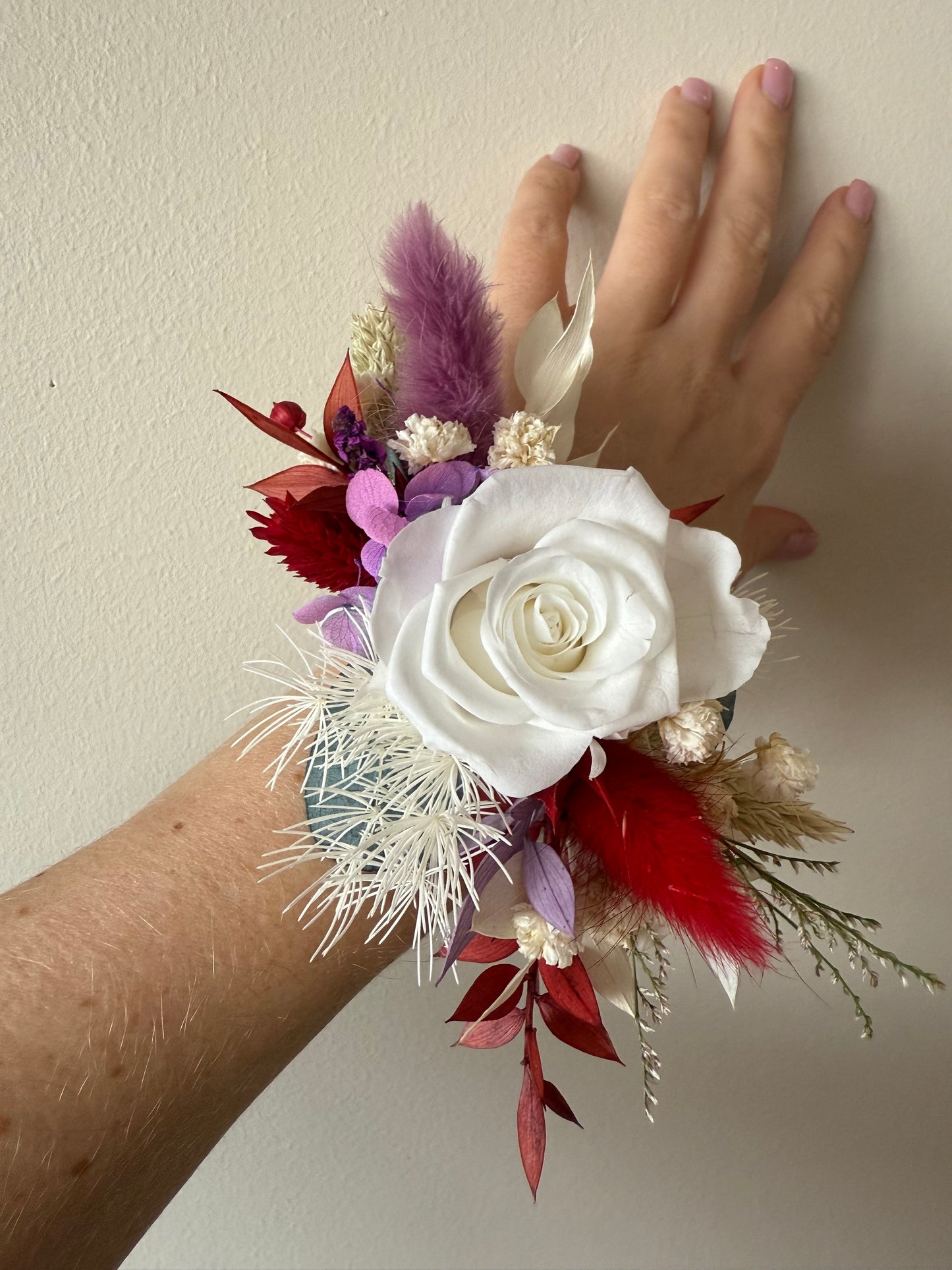 Floral wrist corsage with a white rose and red feathers on a plain background