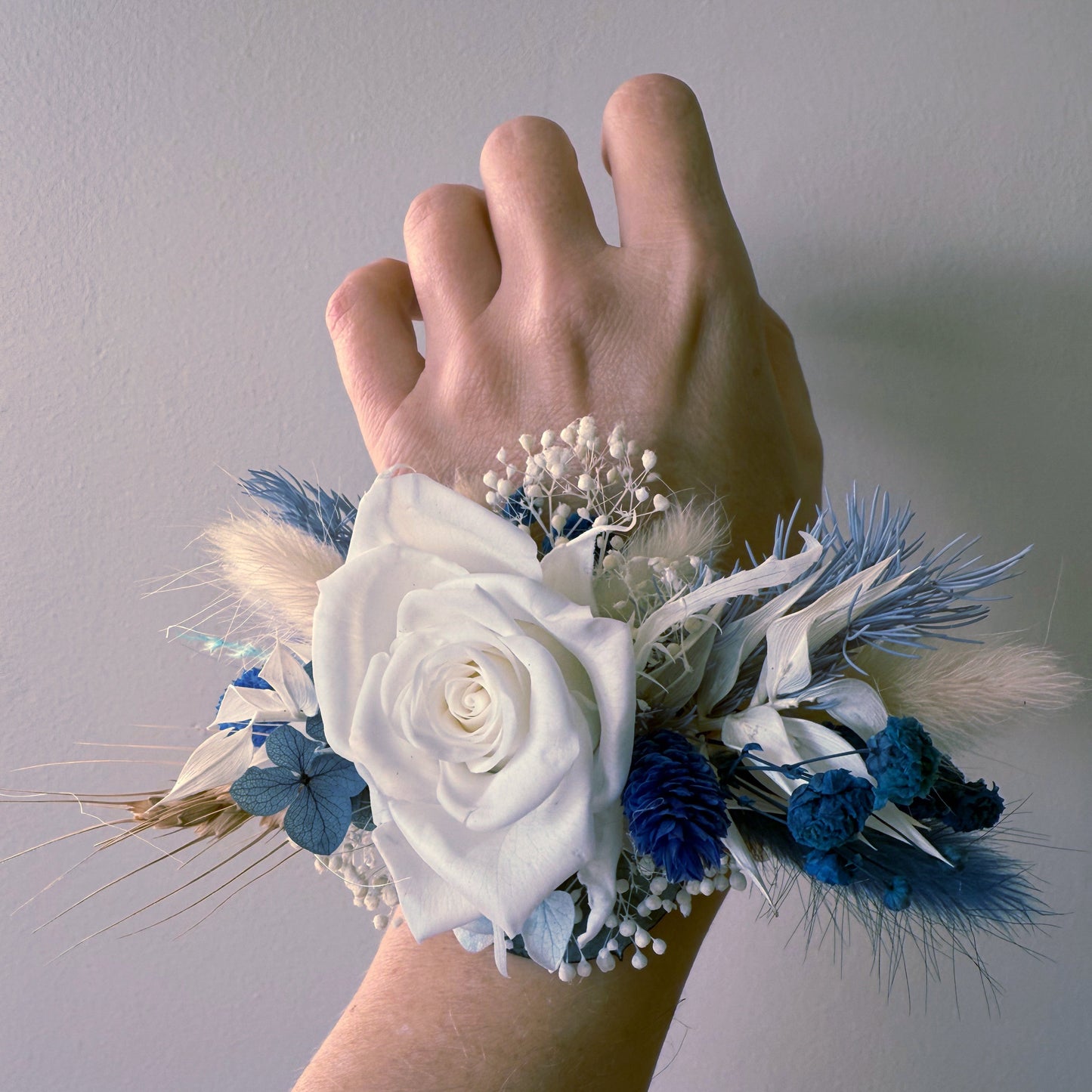 Floral wrist corsage with white and blue flowers on a plain background