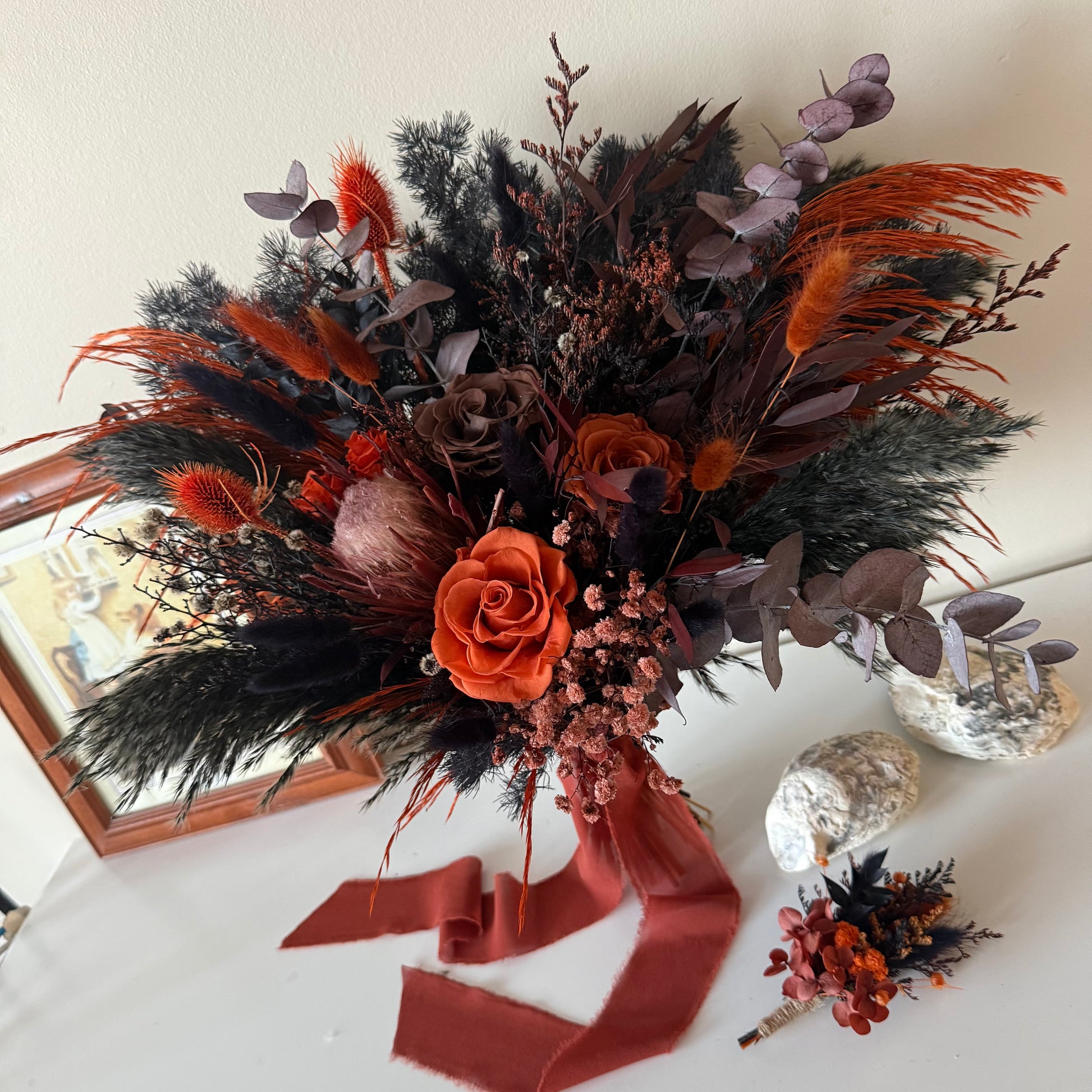 Bouquet of autumnal flowers with orange and brown tones on a white surface.