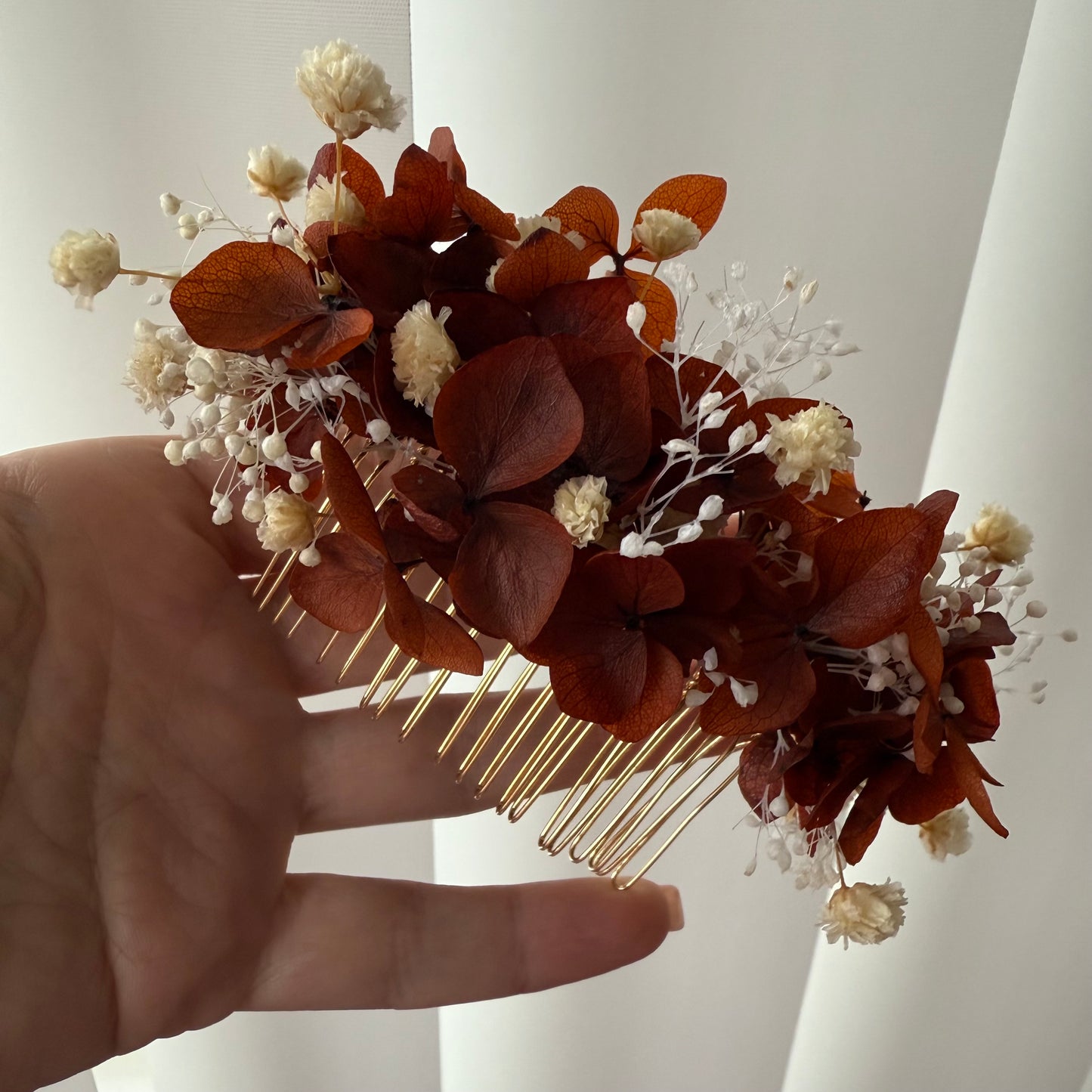 Hair comb with dried leaves and flowers held by a hand against a neutral background