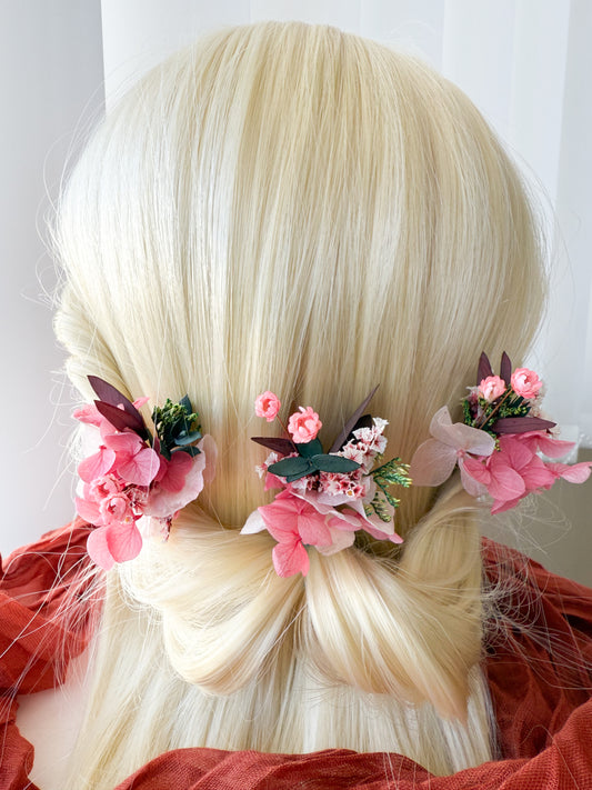 Close-up of wedding hair pins with pink cherry blossom flowers and greenery on a low bun, romantic bridal hairstyle accessory