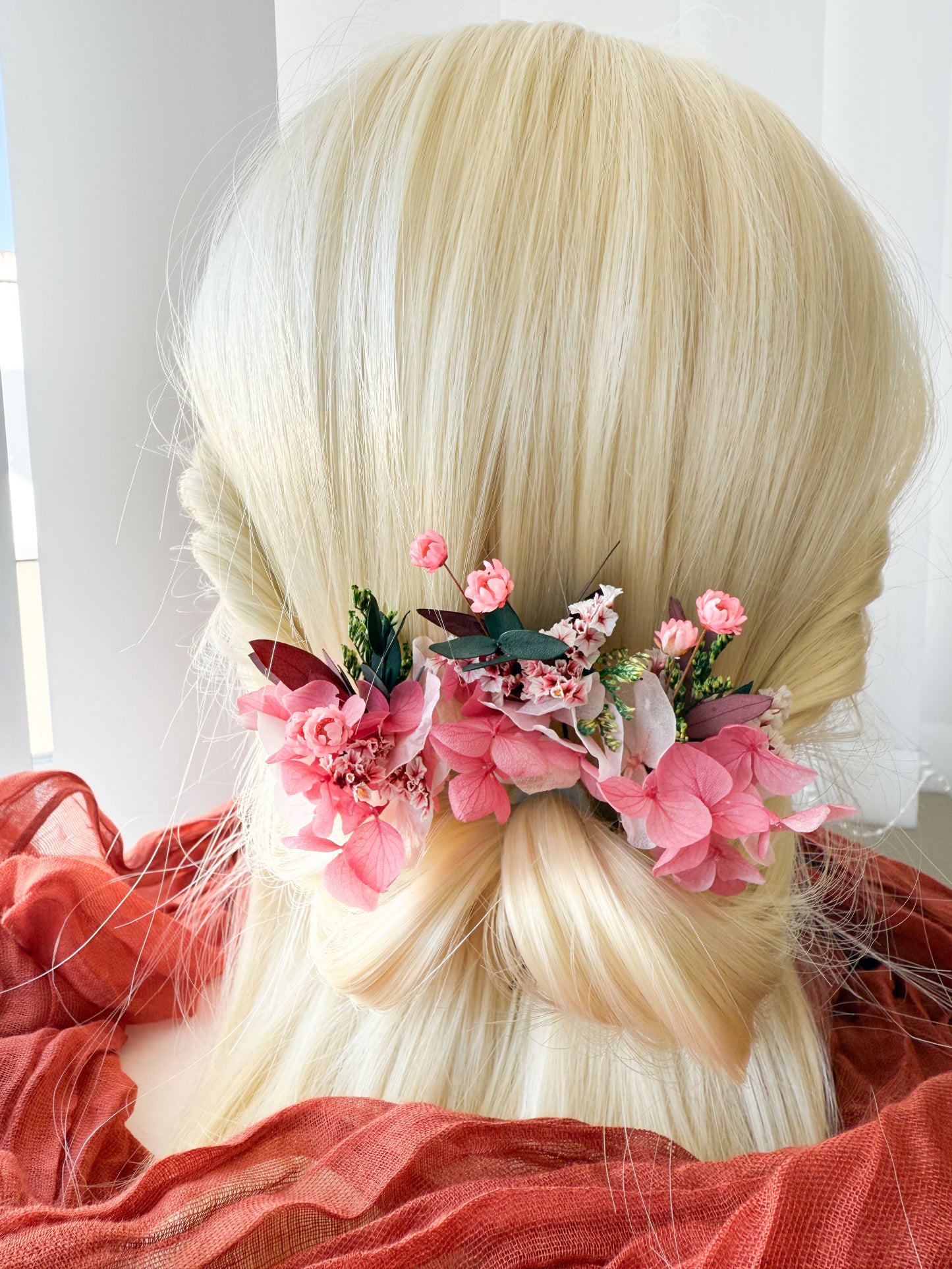 Bridal hairstyle decorated with pink hair flowers arranged symmetrically on both sides of a low bun