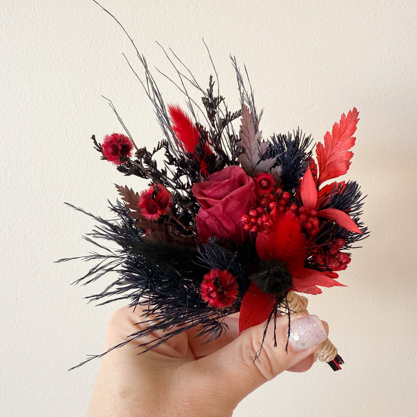 Burgundy rose boutonniere with dried flowers, black details, and rustic twine wrap for gothic wedding