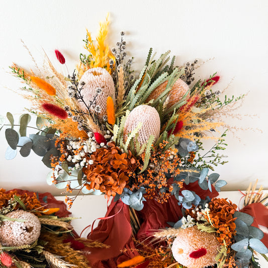Large rustic bridal bouquet with banksia, eucalyptus, hydrangea, bunny tails, and burnt orange dried flowers, styled with a deep red ribbon.