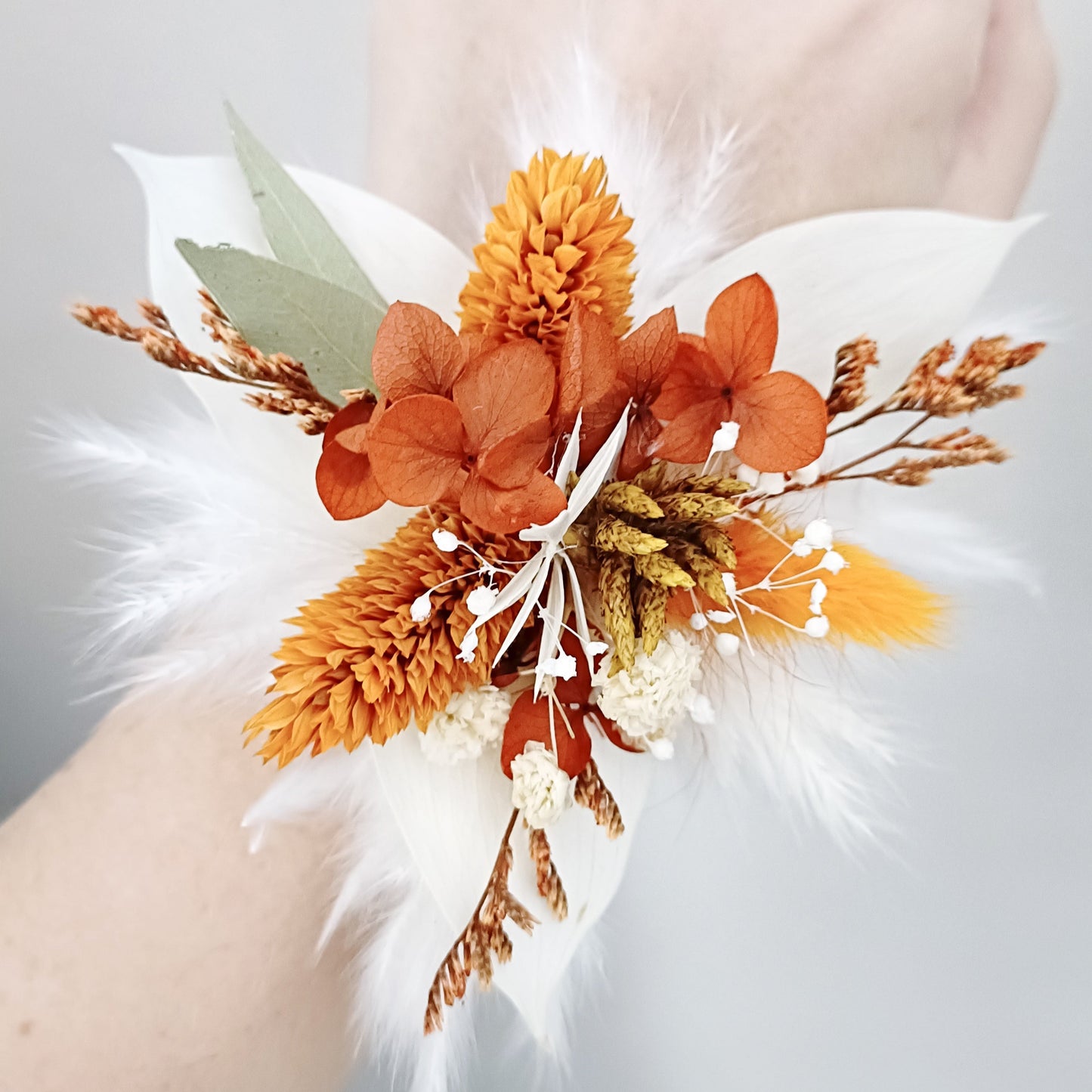 Rustic wedding wrist corsage featuring dried hydrangea, bunny tails, and white feathers