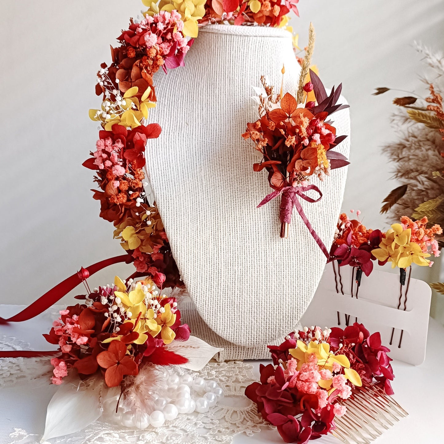 A delicate dried flower crown featuring a bold mix of red yellow & terracotta petals, adorned with tiny pearl accents. The wreath is tied with sheer ribbon, creating an elegant, romantic look for a wedding or special occasion.