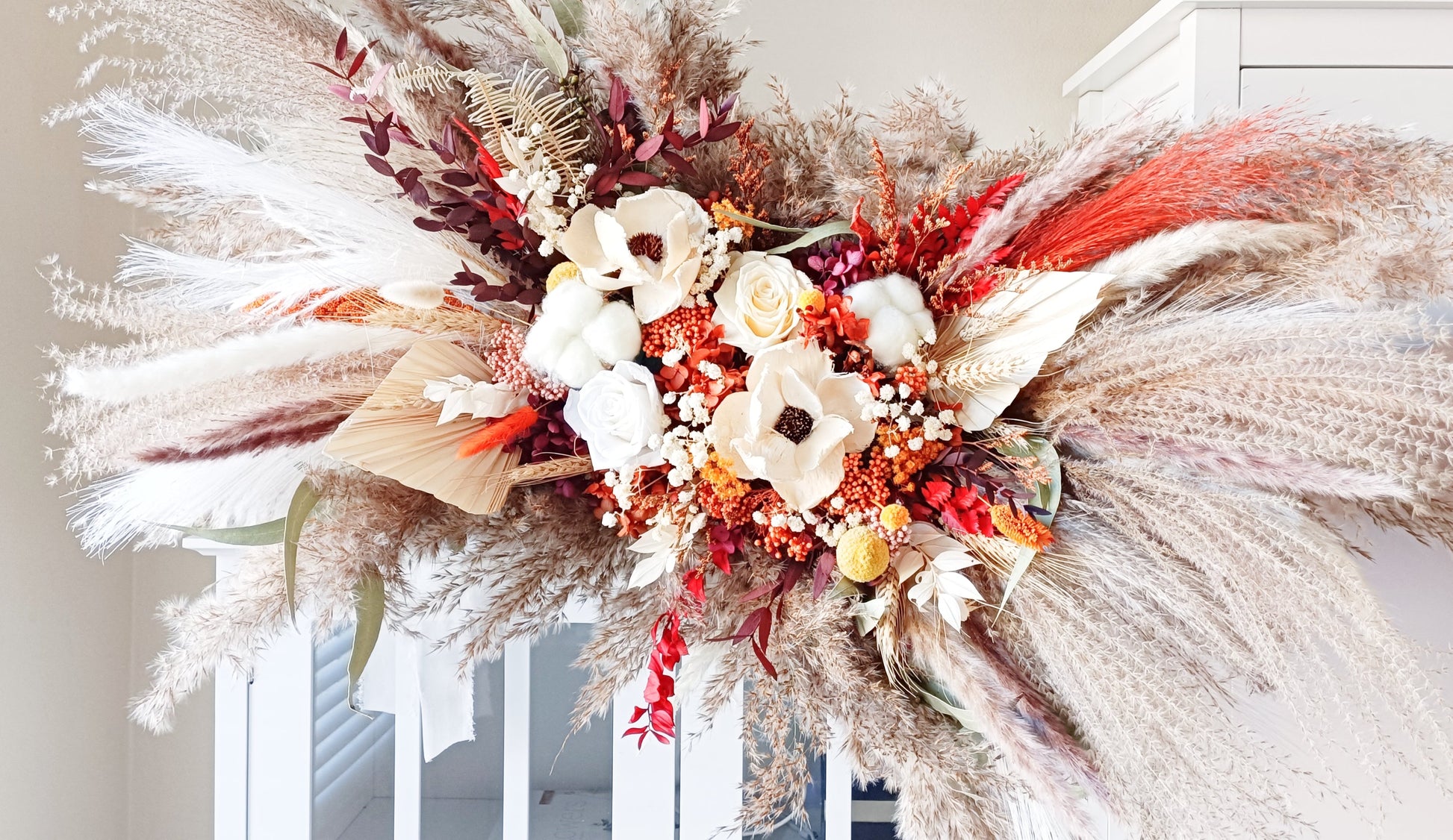 This eye-catching wedding arch flowers features a bold combination of red, orange, and natural hues, crafted from a selection of dried flowers. The arrangement includes pampas grass, preserved foliage, and textured accents, offering a rustic yet vibrant look perfect for autumn weddings. Long-lasting and full of character, this arch arrangement adds a fiery touch to any bridal ensemble. Explore our collection for more unique and seasonal wedding bouquets.