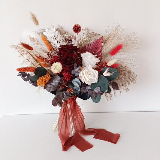 Warm-toned dried flower bouquet in burgundy, ivory and orange, styled for a rustic or bohemian wedding.