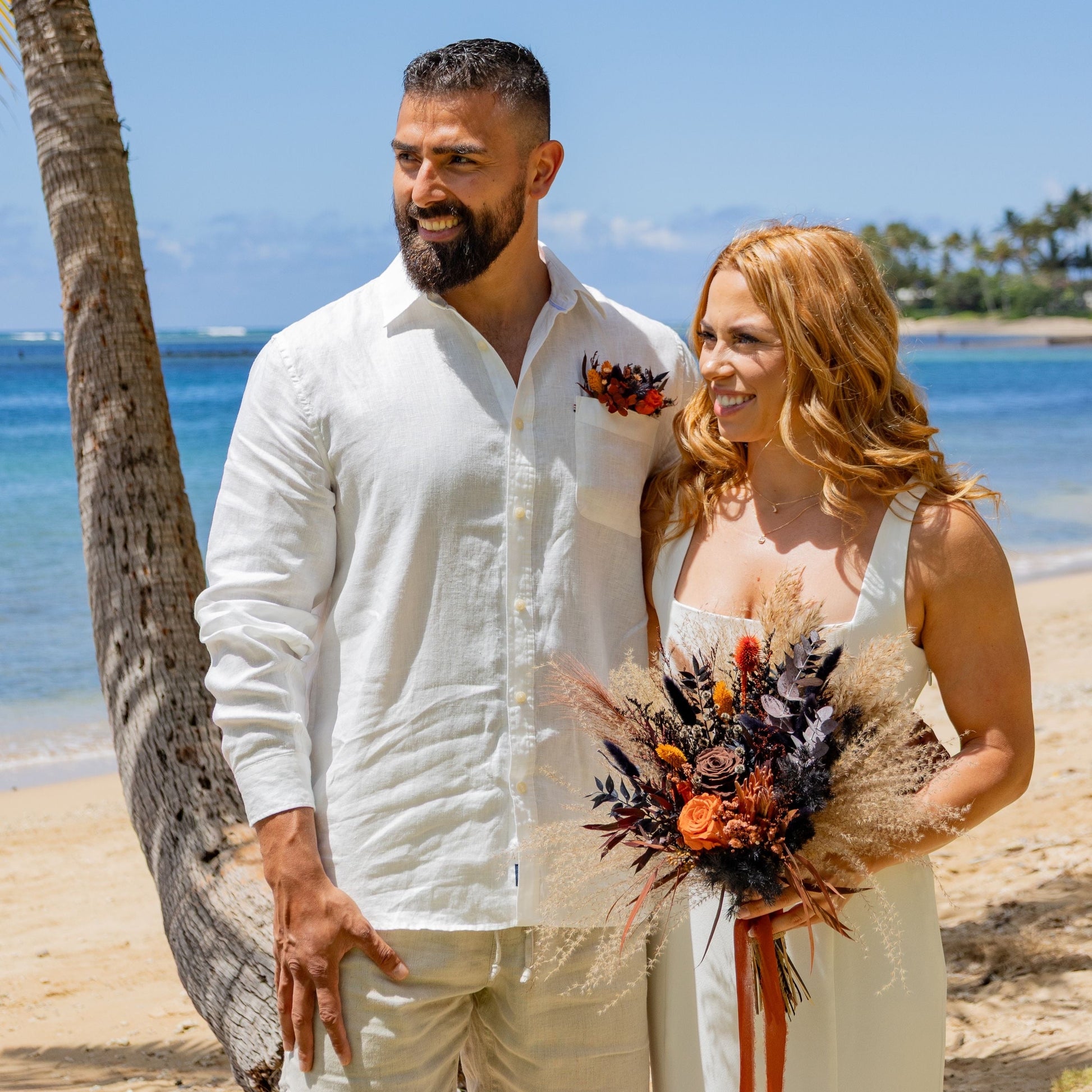 Bride and groom on a tropical beach with boho burnt orange and black dried flower wedding bouquet and matching boutonniere
