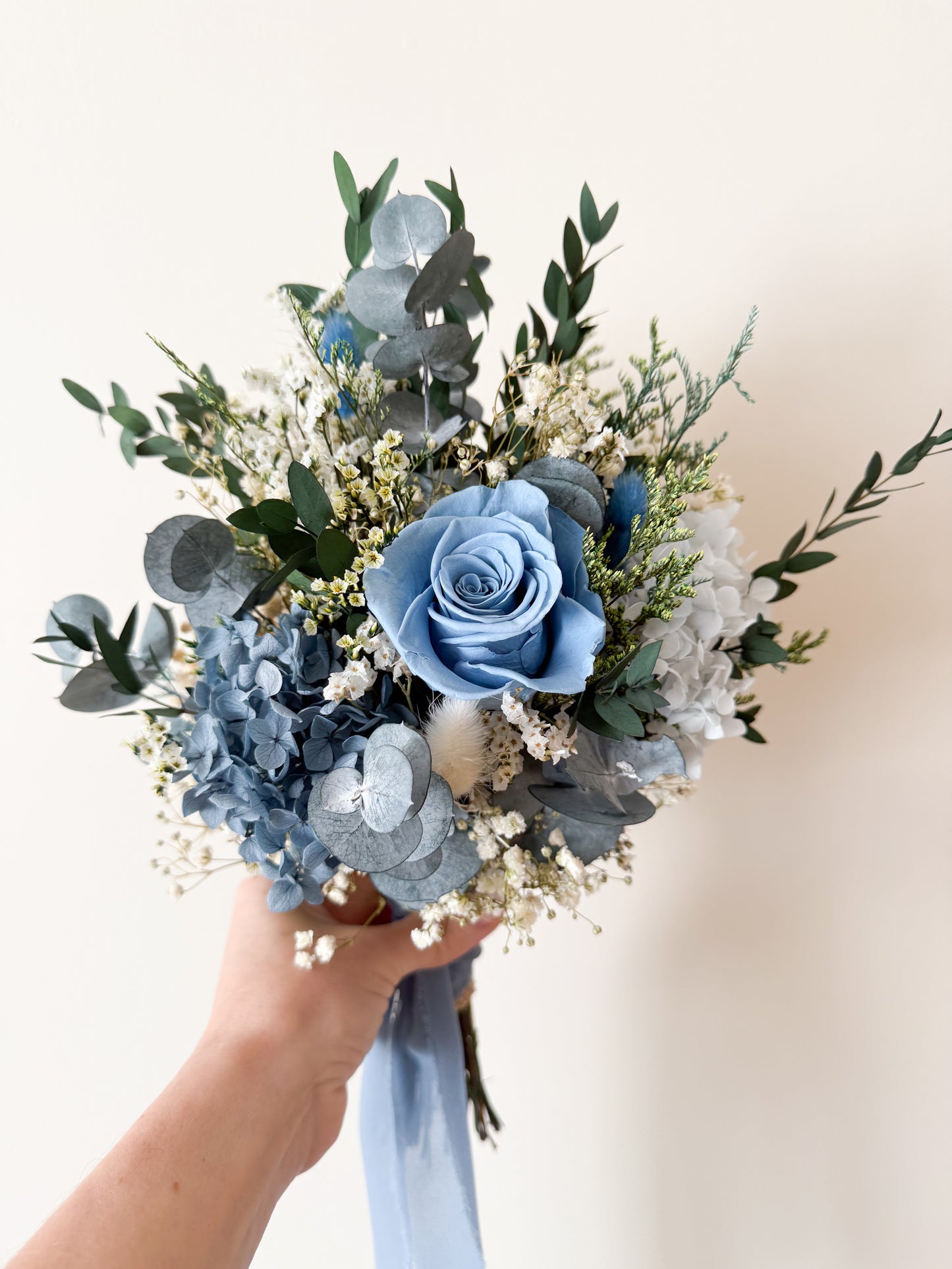 Blue and white dried flower bridal bouquet tied with soft blue ribbon, featuring rustic natural textures for weddings.