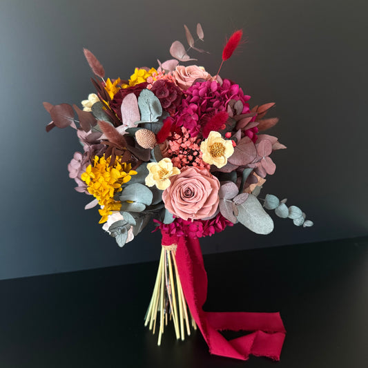 Bohemian style bridal bouquet with burgundy, yellow, and terracotta dried flowers, perfect for modern rustic weddings.