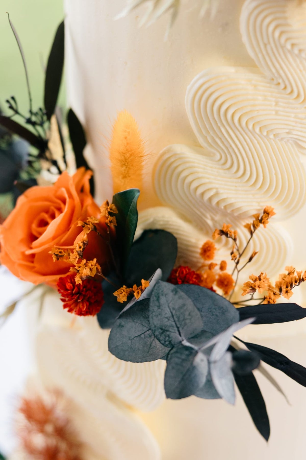 Boho cake flower decorations combining terracotta roses, warm orange blooms and dried foliage, designed for an earthy wedding celebration.