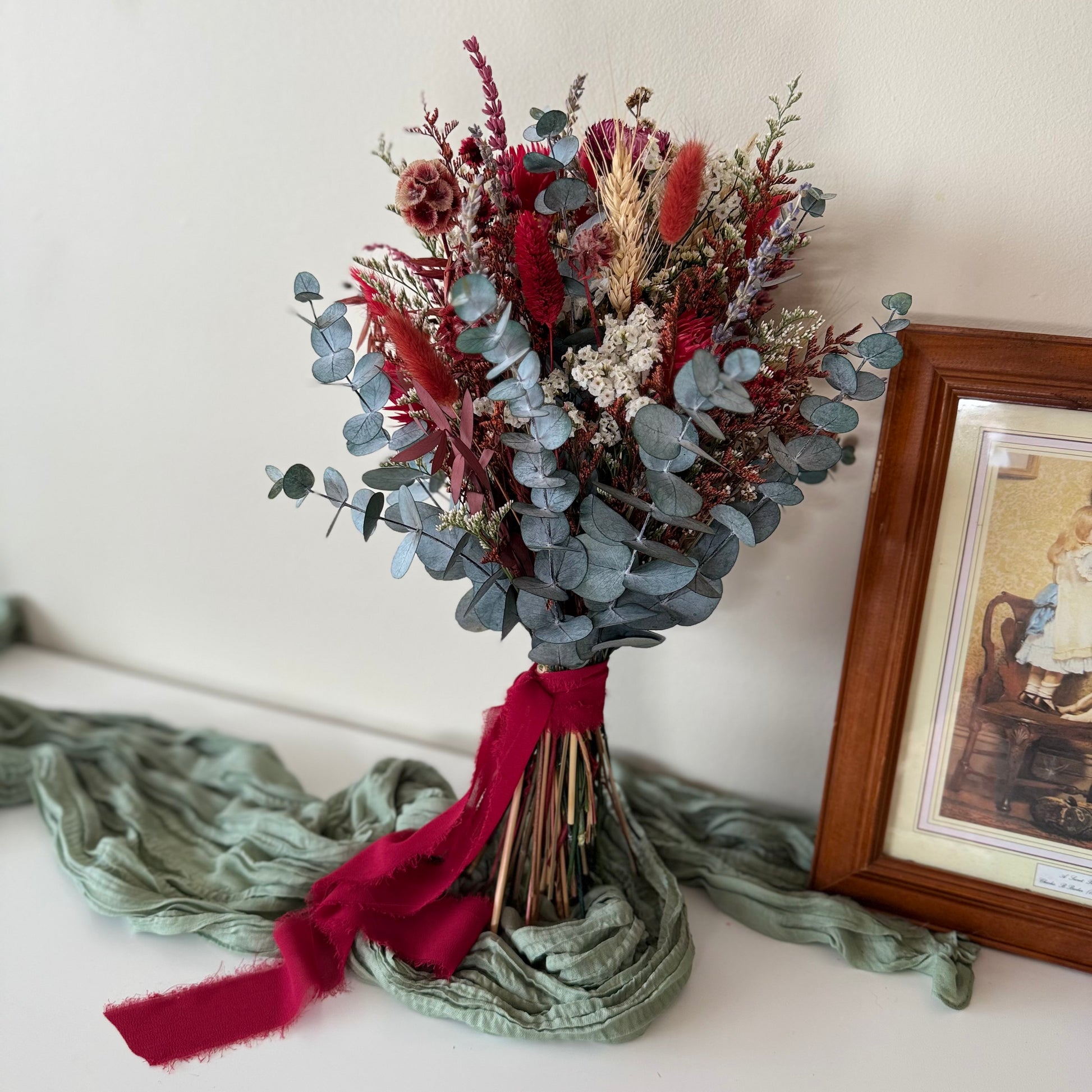Close-up of boho dried bridal bouquet showing red gomphrena, white gypsophila and eucalyptus leaves