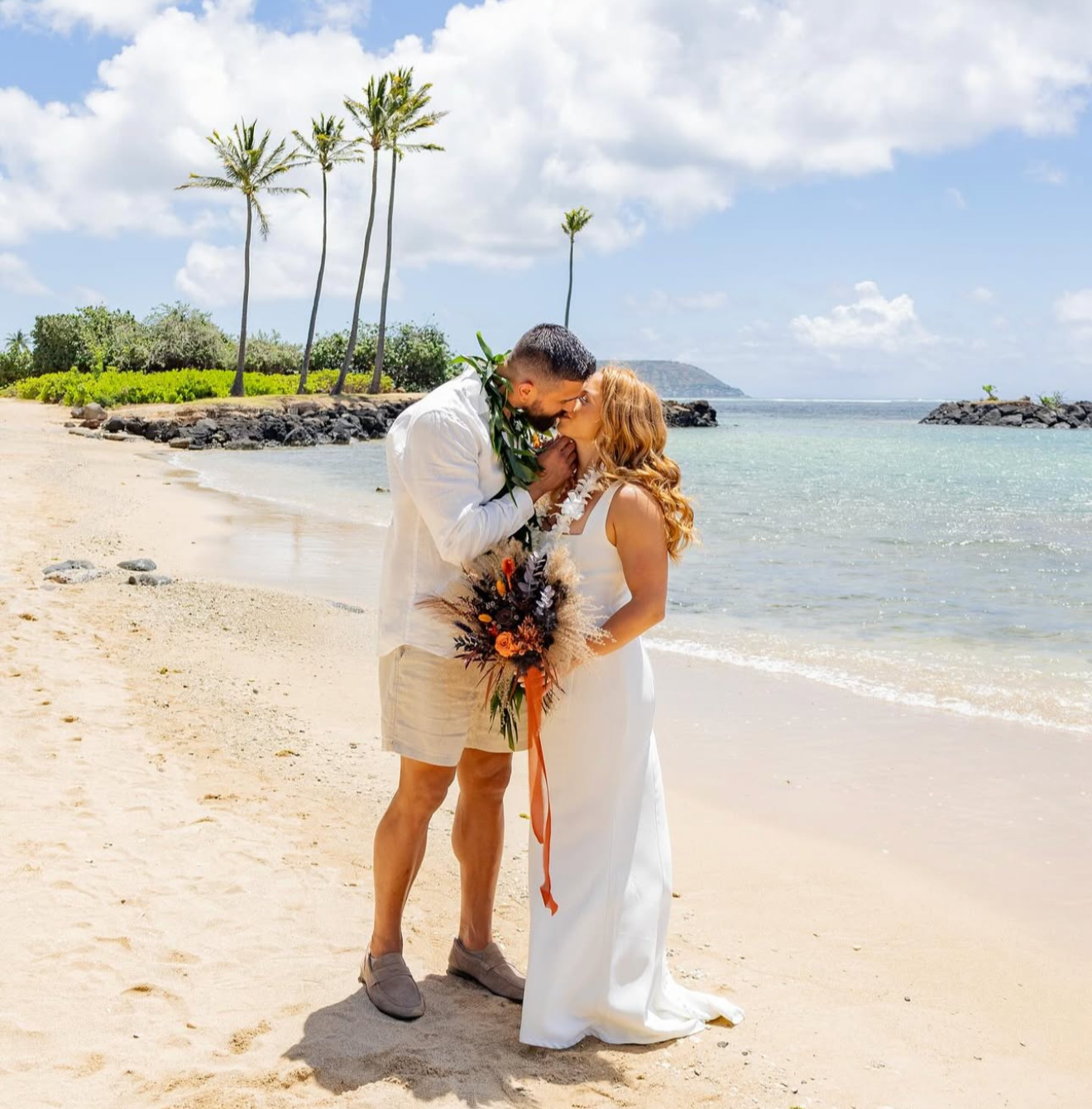 Couple embracing on a beach with palm trees and ocean in the background