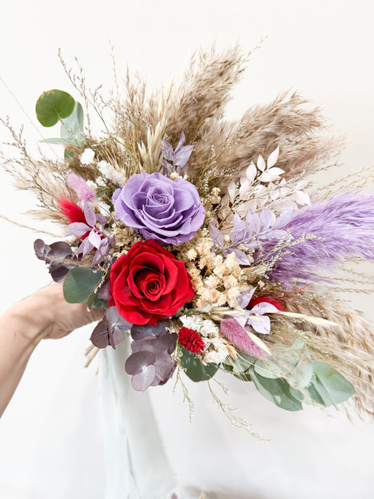 boho bridal Bouquet of flowers with red roses, purple flowers, and pampas grass held by a person.