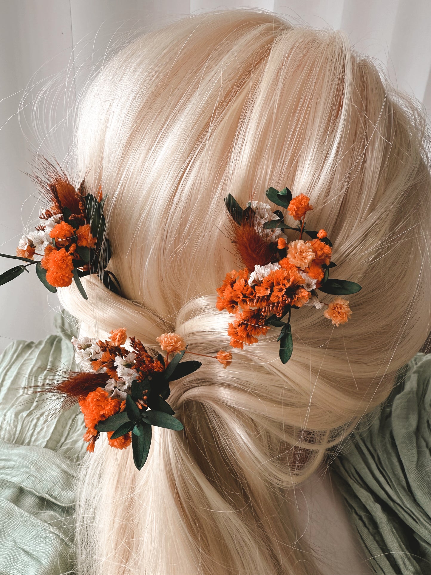 Blonde hair styled with orange flowers and green leaves against a neutral background