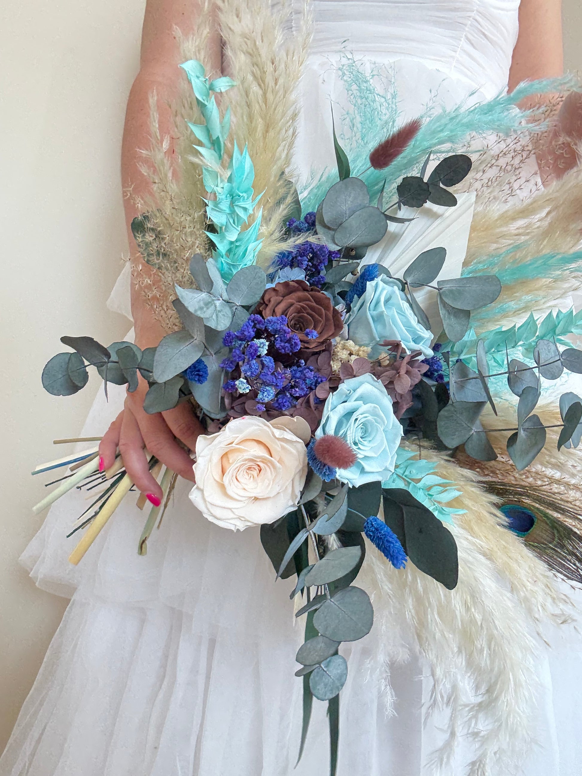 Bride holding teal and navy dried flower bouquet in boho rustic style.