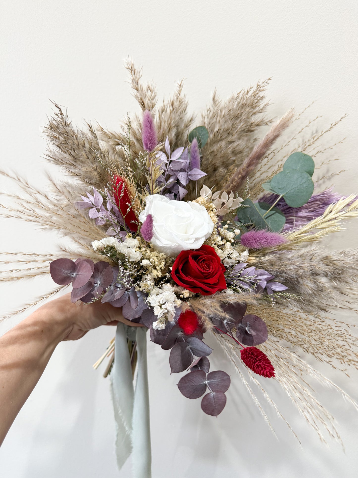bridesmaids Bouquet of flowers with red roses, white flowers, and pampas grass held by a person against a white background