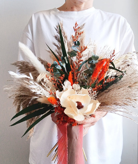 Sola Flower Bouquet with Green Eucalyptus, Pampas Grass, and Orange Hues  Add a touch of natural elegance to any occasion with our Sola Flower Bouquet, featuring green eucalyptus, pampas grass, and vibrant orange hues. Handcrafted with care, this bouquet combines the delicate beauty of sola flowers with the rustic charm of pampas grass and the fresh scent of eucalyptus.