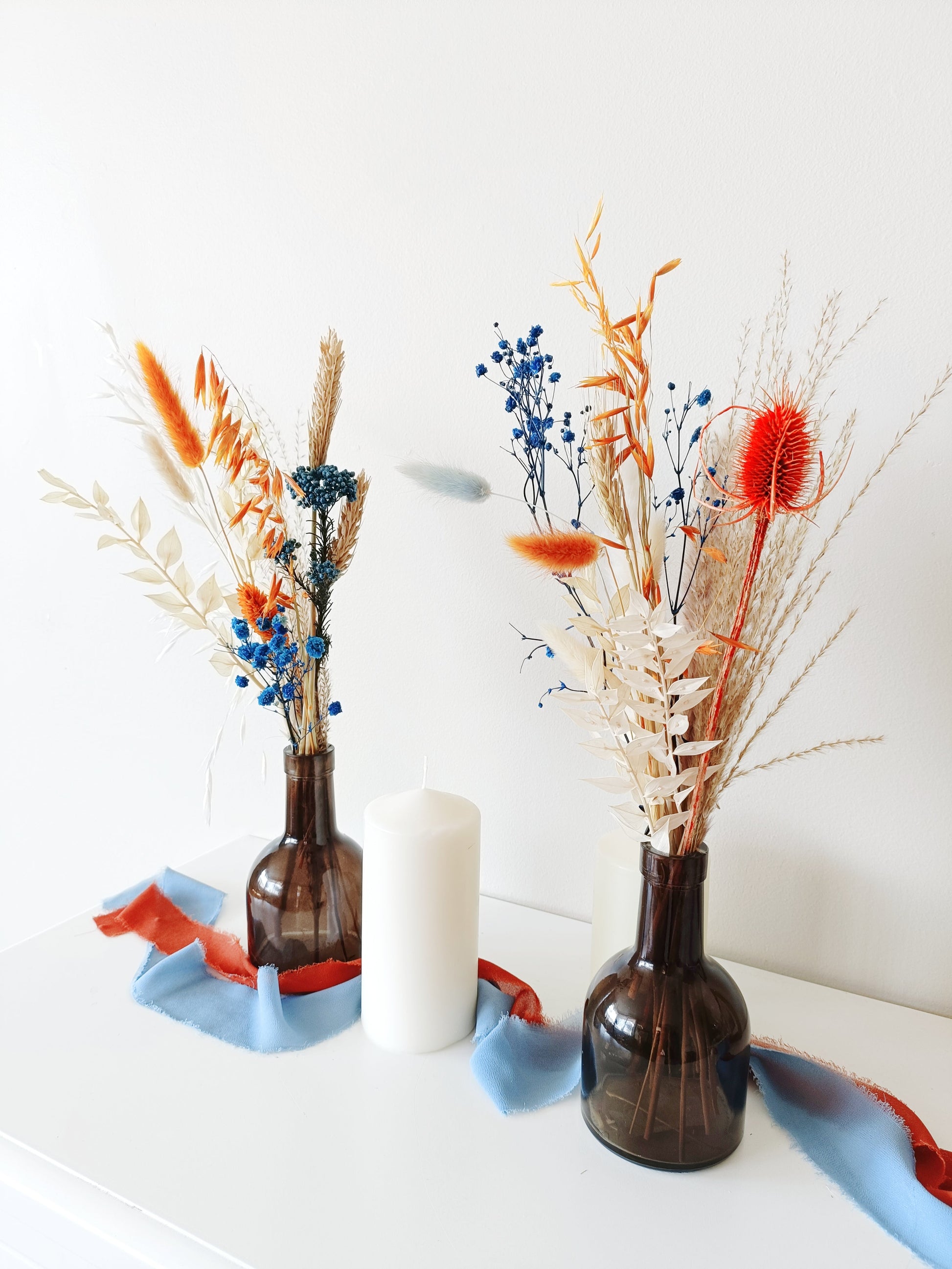 dried flower decor, vibrant floral centerpiece, blue and orange wedding flowers, artistic floral arrangement, striking dried flower setup, colorful wedding decor, preserved flower table display, unique rustic florals, dried flower boho centerpiece, modern botanical decor, vibrant boho styling, energetic floral arrangement, contrast floral table decor, wildflower-inspired setup, bright wedding flowers, dried pampas grass decor, eye-catching floral vase, handcrafted dried bouquet, colorful natural centerpiece