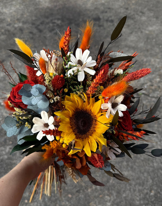 Bouquet of dried flowers including sunflowers and eucalyptus held by a person against a concrete background.