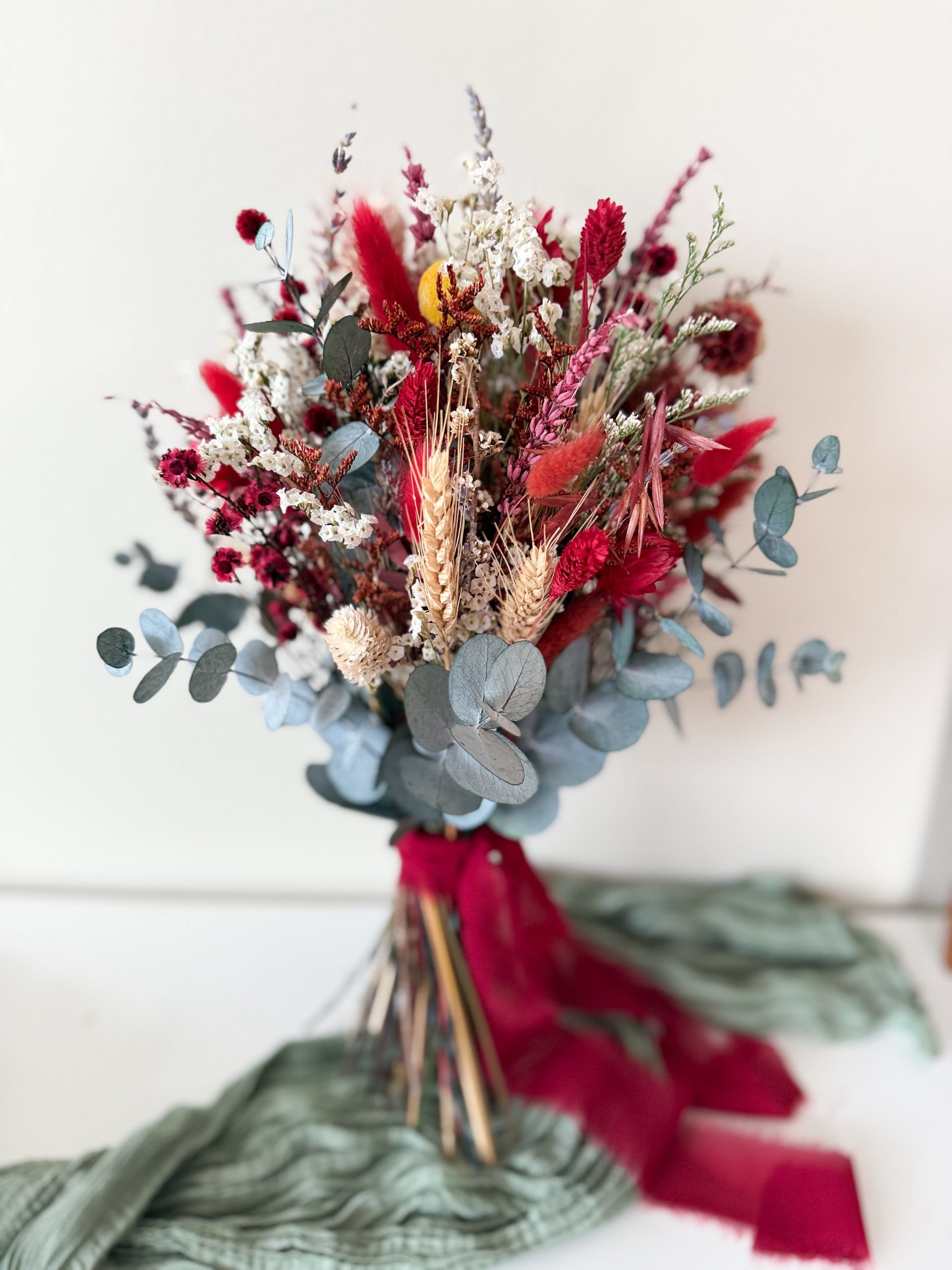 Dried boho wedding bouquet in red, white and blue eucalyptus held against a cream background