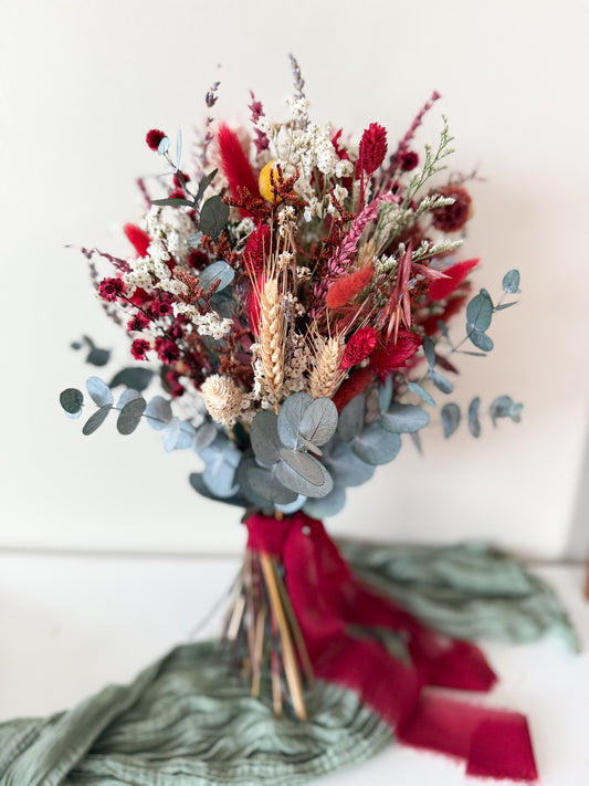 Dried boho wedding bouquet in red, white and blue eucalyptus held against a cream background