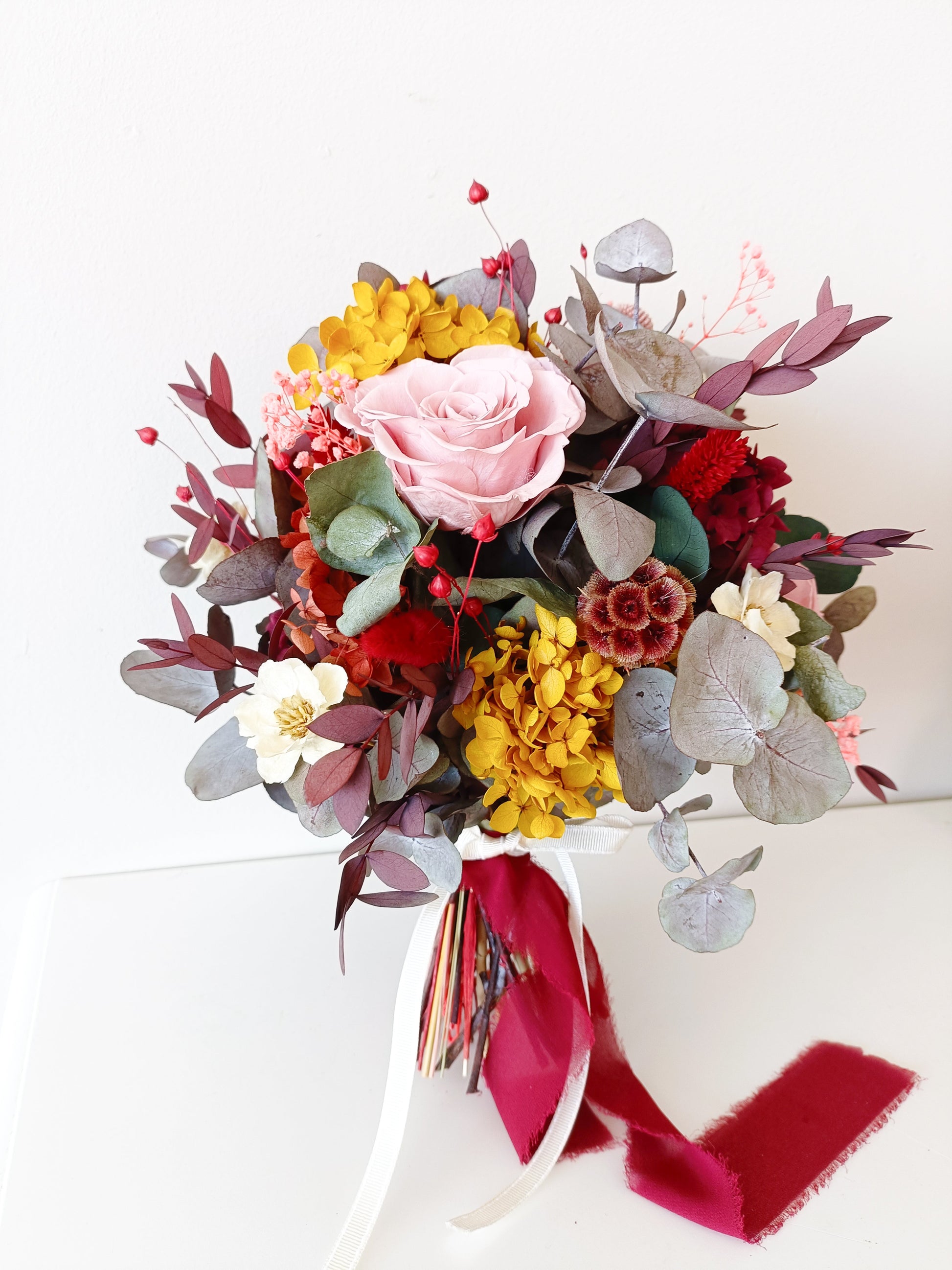 Romantic dried flower bouquet with preserved hydrangea, eucalyptus, ruscus, sola wood flowers and pink preserved roses, styled with velvet ribbon.