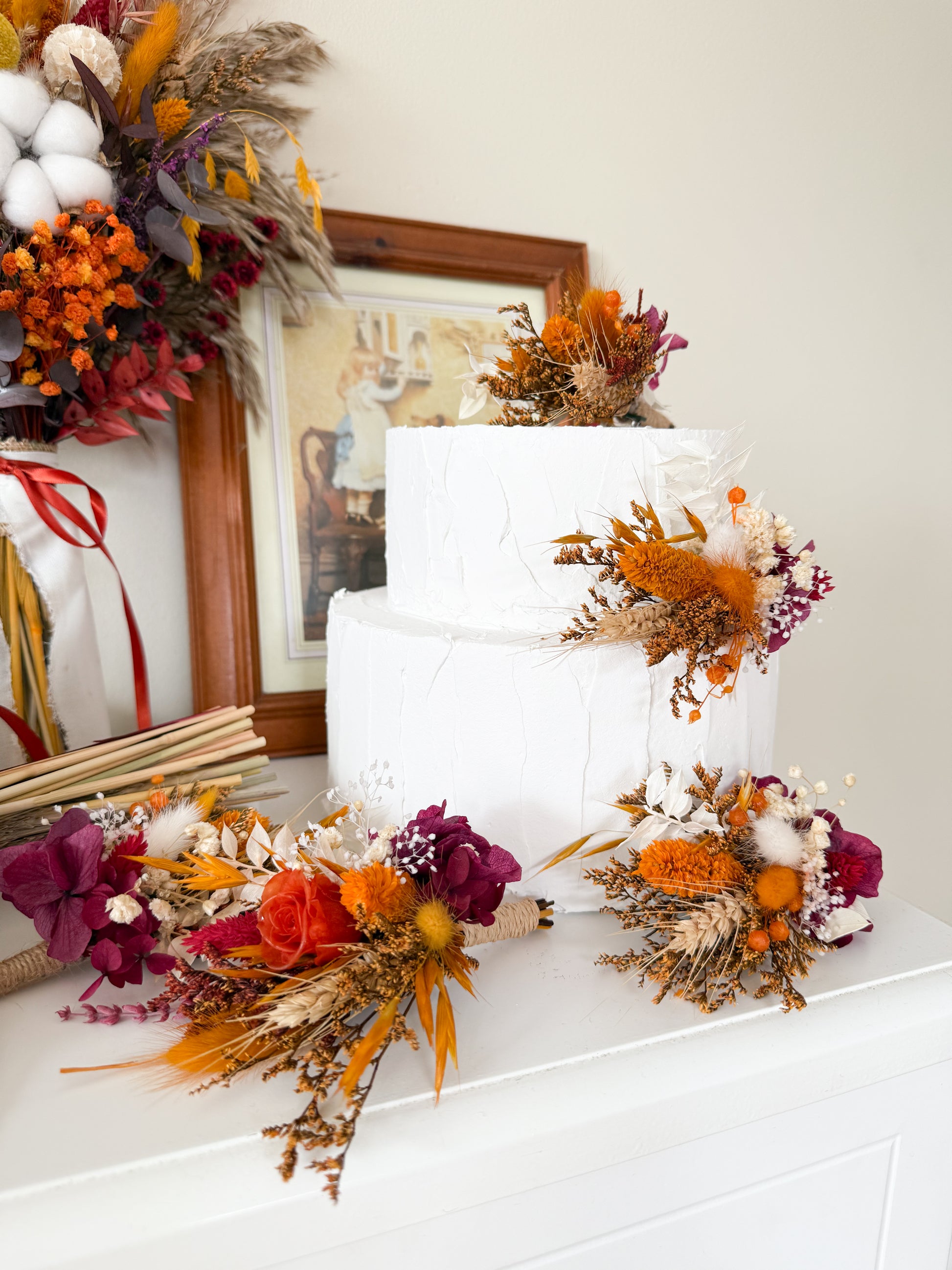 Two-tier white wedding cake decorated with dried flower toppers in terracotta, burnt orange, burgundy, pampas and cotton – rustic boho style
