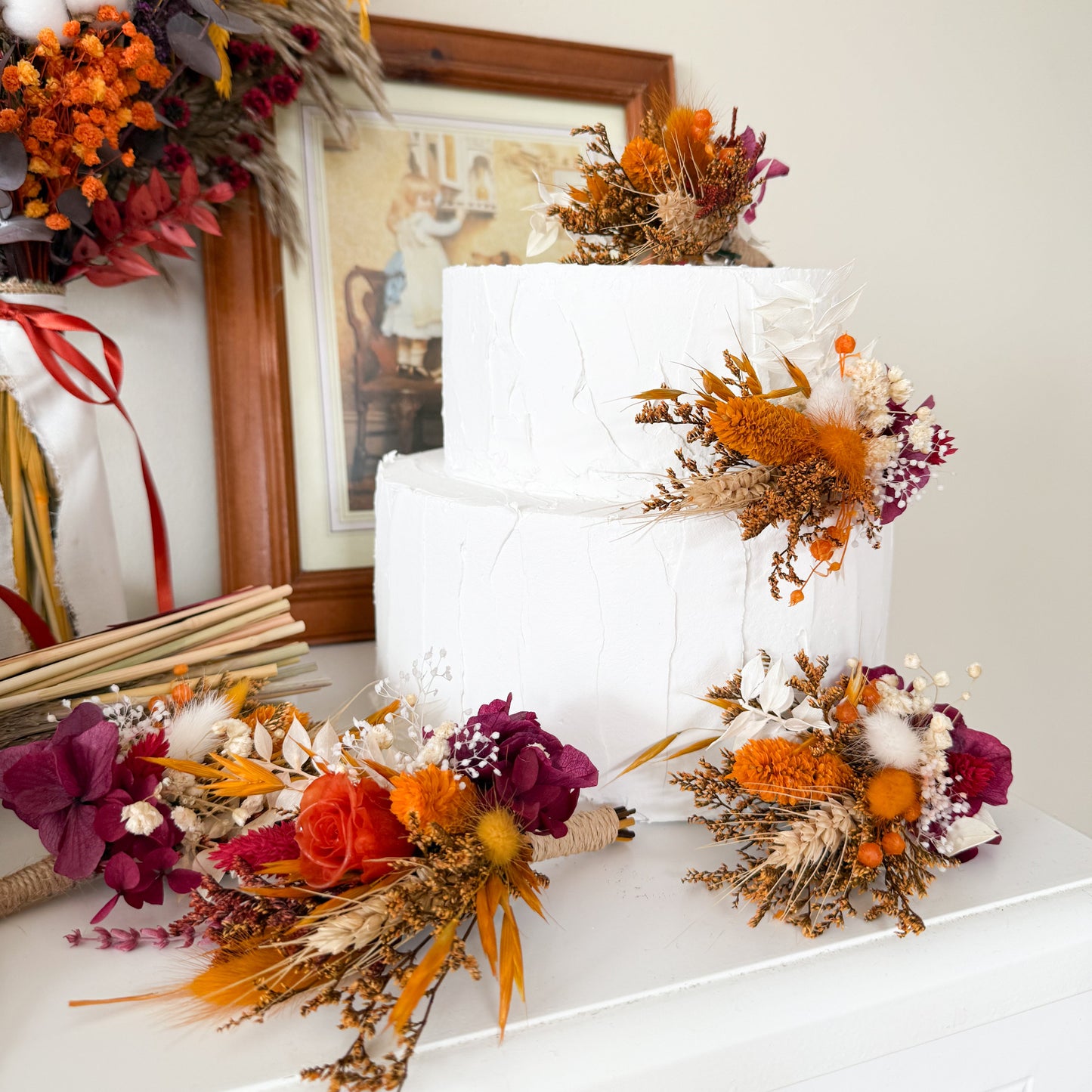 Two-tier white wedding cake decorated with dried flower toppers in terracotta, burnt orange, burgundy, pampas and cotton – rustic boho style