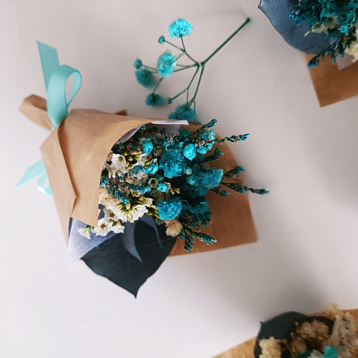 Close-up of preserved teal dried flower bouquet with natural paper wrap and eco ribbon.