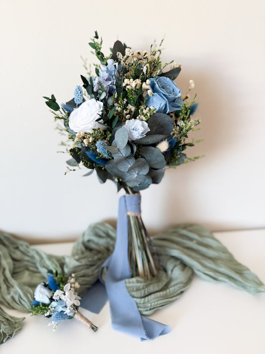 Dusty blue boho bridal bouquet with preserved roses, ivory accents, and eucalyptus, tied with a soft silk ribbon for a modern rustic wedding.